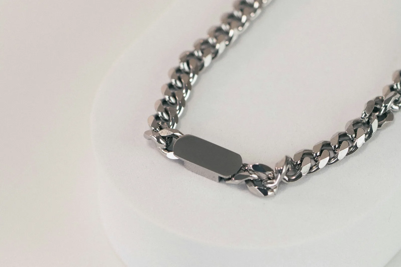 Collier gourmette en acier inoxydable argenté avec plaque, posé sur un fond clair